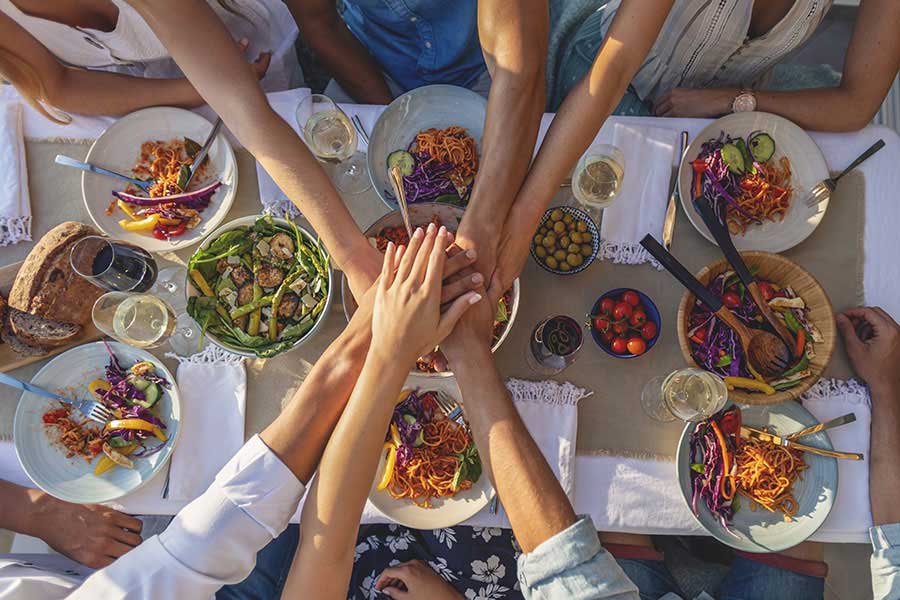 Group of people sitting around a table with their hands together eating a well-balanced meal.
